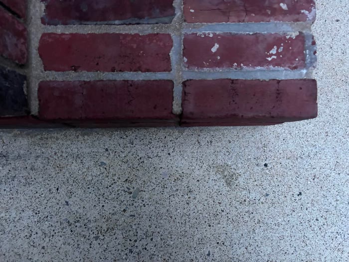The corner of a red brick step sitting on speckled, freshly cleaned concrete.
