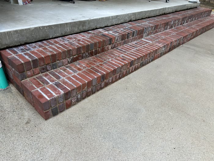 Two red brick steps running along the edge of a concrete porch, above a clean concrete walk.