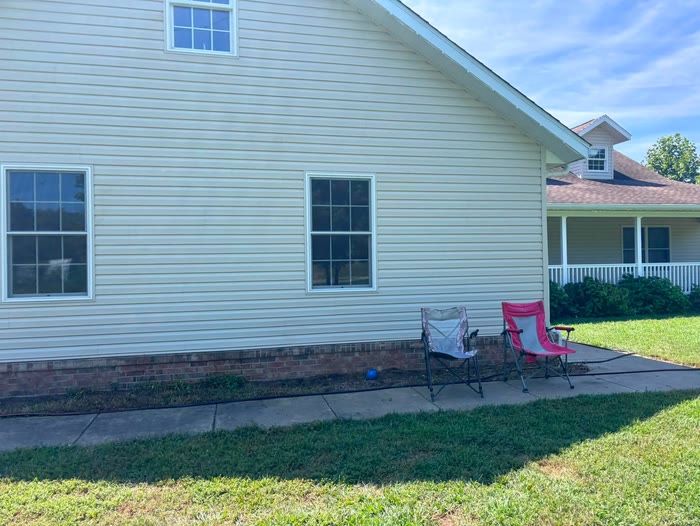 The long side of a house with clean siding and two windows, two camp chairs on the path and a lawn in front.