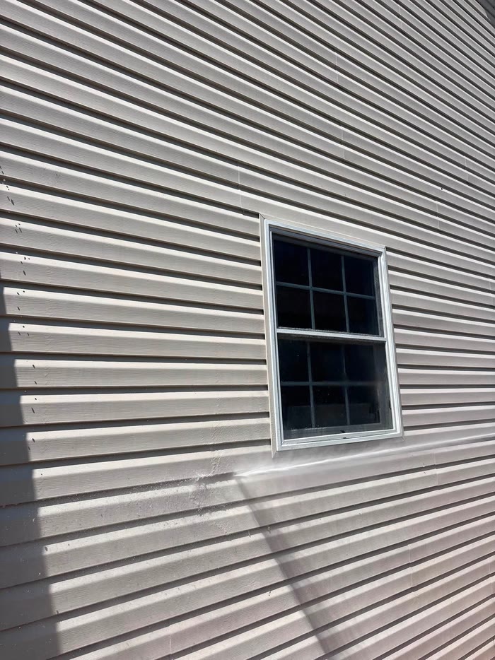 Looking along clean pale siding toward a single window, the panels lit by low sun.