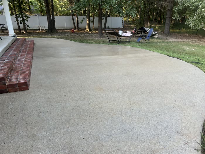 A wide curved concrete patio, clean and even in colour, with lawn chairs and trees behind it.