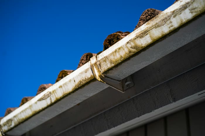 A white gutter streaked with dirt below the edge of a roof, against a deep blue sky.