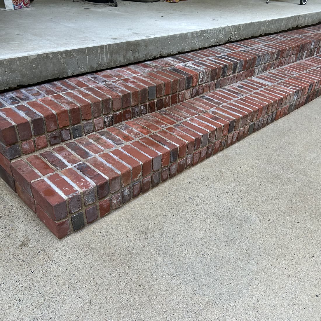 Two red brick steps running along the edge of a concrete porch, above a
                    clean concrete walk.
