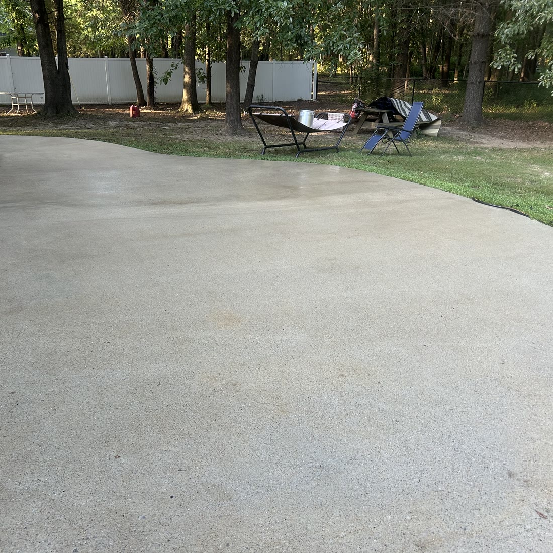 A wide curved concrete patio, clean and even in colour, with lawn chairs
                    and trees behind it.